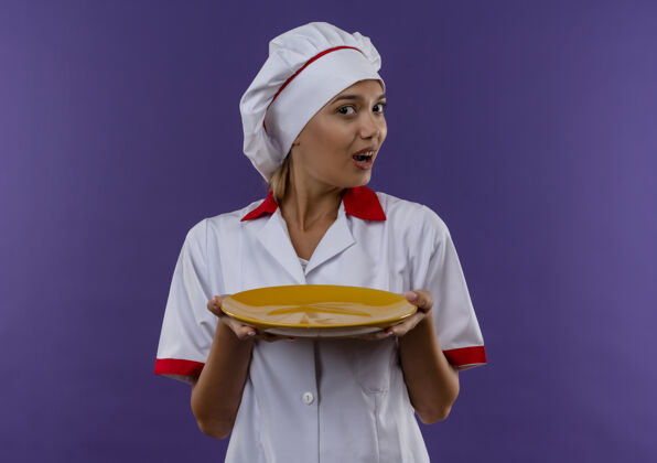 女惊讶的年轻厨师女身穿厨师制服举行孤立的背景与复制空间板穿着制服盘子