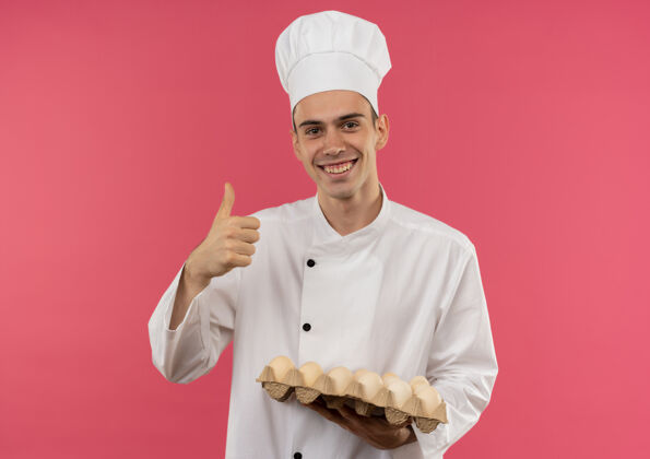 男性面带微笑的年轻男厨师穿着厨师制服 举着一批鸡蛋 大拇指朝上向上厨师鸡蛋