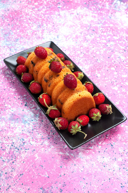 饼干正面是美味的烤蛋糕 放在黑色的蛋糕锅里 粉红色的桌子上放着新鲜的红色草莓黑色水果甜点