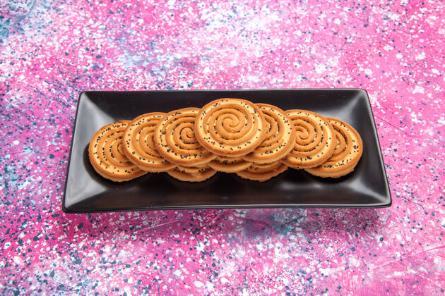 金色前视图甜甜的饼干美味的小饼干里面黑色的形式在淡粉色的桌子上黑色小糖果