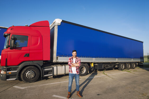 卡车司机穿着休闲服和靴子的职业美国卡车司机的肖像站在卡车前面 拖车很长转向卡车司机集装箱