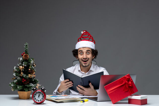 商人年轻的商人惊讶地戴着滑稽的圣诞老人帽子 在黑暗的背景下检查办公室文件中的信息帽子办公室电脑