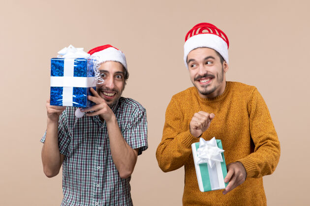 微笑正面图两个戴着圣诞帽的快乐的家伙在米色的背景上展示他们的礼物成人风景圣诞老人