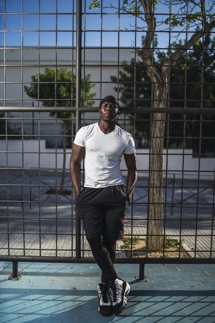 户外一个穿着白衬衫的非洲裔美国男性斜靠在栅栏上的垂直镜头非裔美国人身体黑色