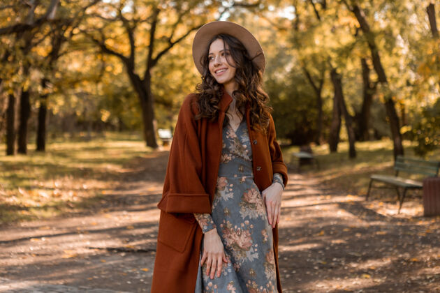 优雅迷人时尚微笑的女士 卷发漫步公园 身着印花连衣裙和保暖外套 秋季时尚 街头风格时尚穿着休闲