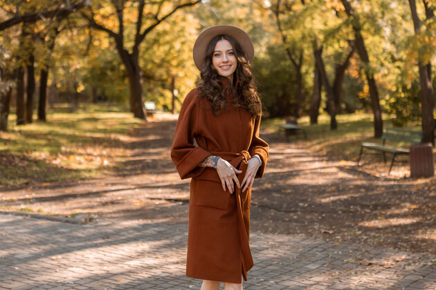 女性迷人时尚微笑的瘦身女子卷发漫步公园身着暖棕色外套 秋日时尚街头风配饰服装秋天