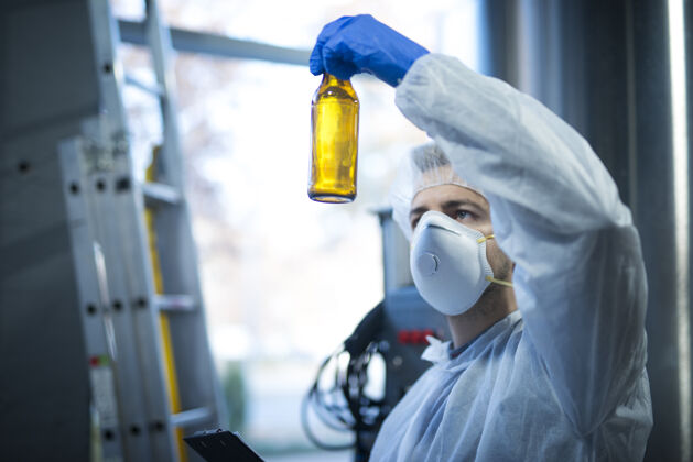 记录啤酒生产厂的技术专家拿着玻璃瓶检查质量瓶子面罩生产