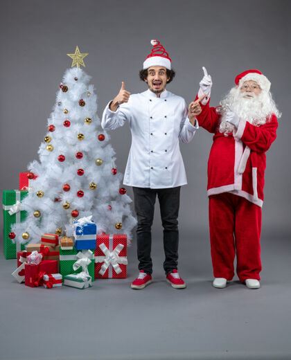 厨师圣诞老人和男厨师在灰色墙上围着圣诞礼物的正视图快乐圣诞老人人们