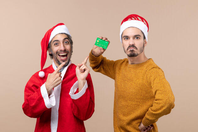 男前视图两个家伙 一个穿着圣诞老人外套 另一个手放在米色隔离背景的腰部两个家伙外套男人