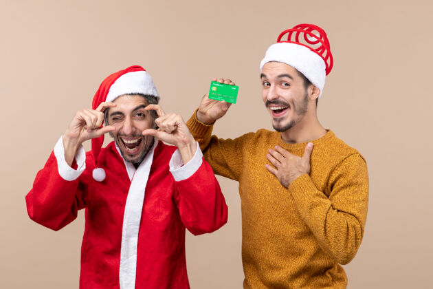 伙计们正面图两个快乐的家伙 一个穿着圣诞外套 另一个手放在胸部 背景是米色的米色成人视图