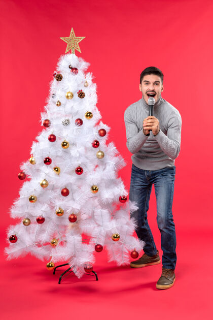 男孩圣诞气氛积极的家伙穿着牛仔裤站在装饰圣诞树附近 热情地唱歌礼物庆祝心情