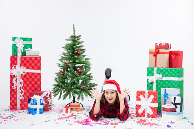 装饰年轻女子躺在白色墙壁上的圣诞礼物和小圣诞树周围的正视图小圣诞树前面