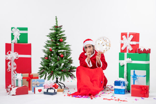 季节圣诞气氛与年轻的圣诞老人坐在圣诞树和礼物在白色背景上不同的颜色礼物年轻礼物
