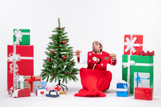 礼物圣诞老人坐在地上 在礼物旁边展示圣诞袜 白色背景上装饰圣诞树 喜庆的节日气氛礼物装饰圣诞老人