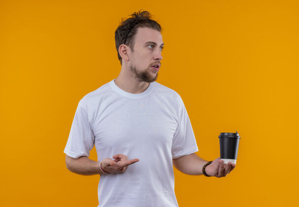 手看着身边穿着白色t恤的年轻人指着咖啡杯 他手上孤立的橙色背景看杯子白色