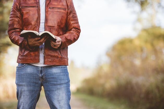 页面男人穿着皮夹克站在一条空荡荡的路上 用模糊的空间读圣经坐着智慧学习
