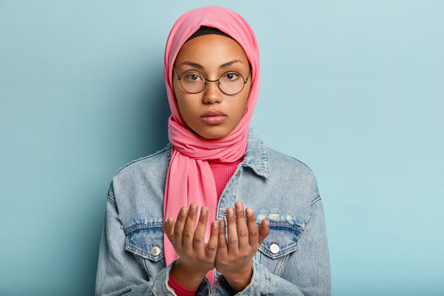信仰严肃的年轻黑皮肤女人看着镜头 在室内祈祷 保持双手祈祷的姿势集中伊斯兰眼镜