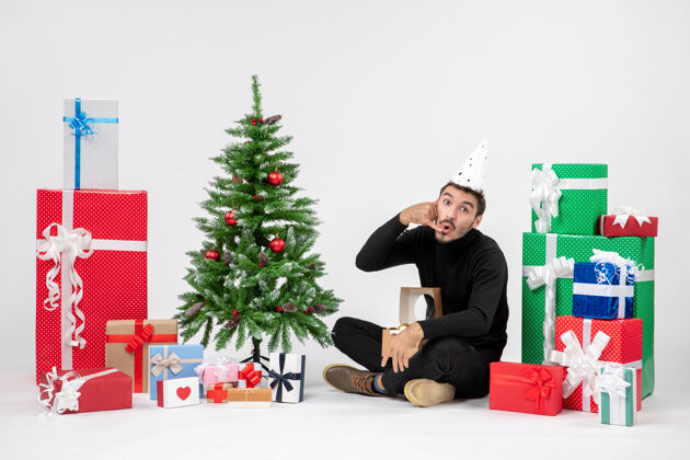 人年轻人坐在白色墙上的节日礼物周围的正面视图礼物快乐盒子
