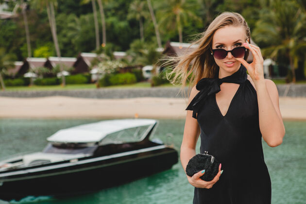 摆姿势奢华性感迷人的女人穿着黑色礼服在豪华度假酒店的码头上摆造型 戴着墨镜 暑假 热带海滩女孩海洋优雅