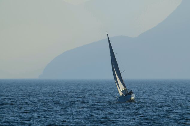 运输小帆船在白天被大雾笼罩的群山环绕的海面上航行山海岸船