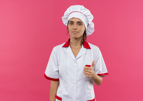 女穿着厨师制服的年轻女厨师高兴地把大拇指竖起放在有复印空间的粉红色隔离墙上年轻拇指制服