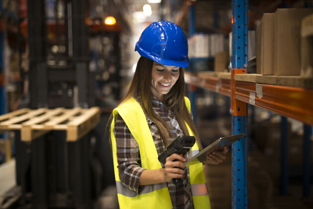 货物微笑的女工手持平板电脑和条形码扫描器在配送仓库检查存货现代职业室内