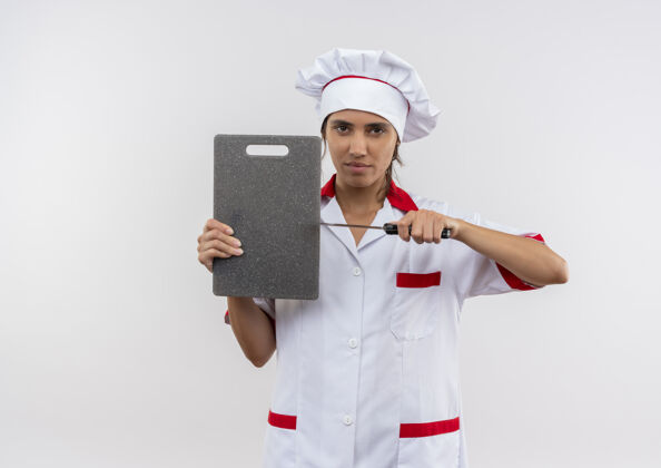 看年轻的女厨师穿着厨师制服拿着砧板和刀站在隔离的白色墙壁上 有复印空间切厨师板子