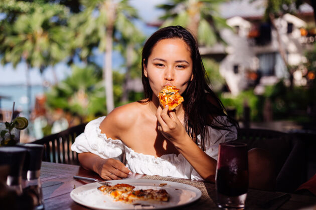 面团快乐的亚洲美女在阳光明媚的日子里饿着肚子吃披萨在户外餐厅日落的阳光下女人在享受美食在午餐的乐趣餐厅美食放松