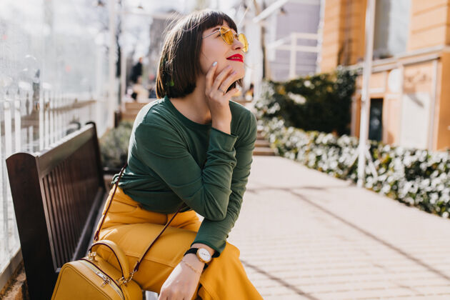 人迷人的棕色头发的女孩穿着绿色毛衣在长凳上冷户外肖像华丽的女士戴着墨镜在街上梦幻的姿势休闲配饰女士