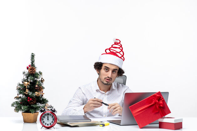 微笑忙碌的年轻商人戴着有趣的圣诞老人帽子在白色背景的办公室里庆祝圣诞节女士商人笔记本电脑