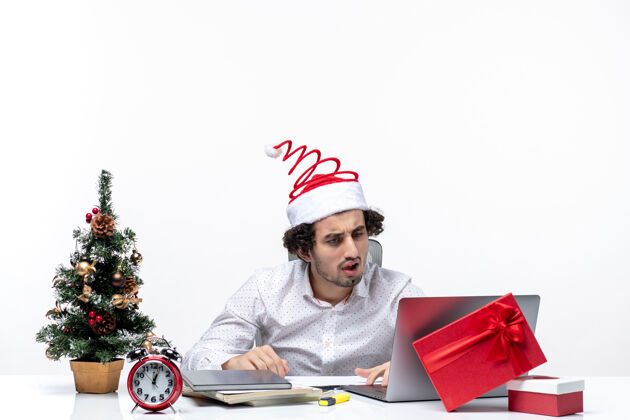 圣诞老人困惑的年轻商人戴着滑稽的圣诞老人帽子 在白色背景的办公室里用笔记本电脑查看邮件成年人微笑帽子