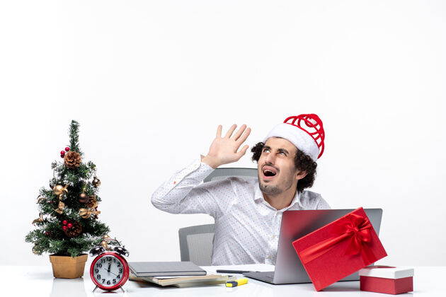 电脑愤怒震惊的年轻商人戴着滑稽的圣诞老人帽子 在白色背景的办公室里向上看人圣诞节年轻商人
