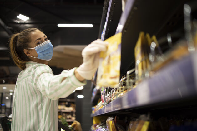 购物车戴着口罩和手套在超市买食物的女人流行病穿着食品杂货店