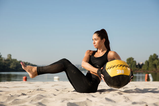 身体年轻健康的女子在沙滩上用球训练上身健美运动员健身肌肉