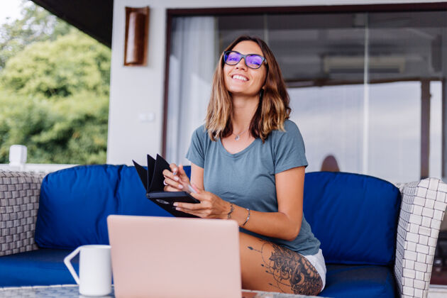 电脑人快乐的白种女人在家里用笔记本电脑做远程工作舒服的地方喝茶朋友女性朋友电脑