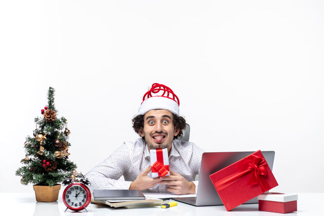 舌头圣诞气氛与年轻的商人圣诞老人帽子和举行他的礼物伸出舌头在白色的背景圣诞老人举行坚持