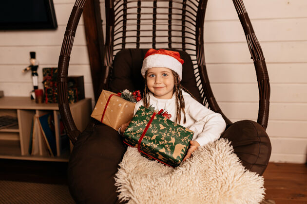 摆姿势快乐的小女孩戴着圣诞帽摆圣诞礼物生活扶手椅帽子