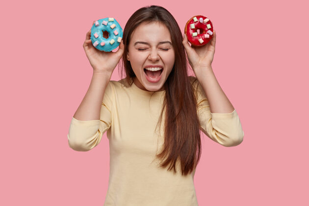 情绪快乐兴奋的女士从幸福中惊呼 端着两个蓝红色的甜甜圈 有时间吃它 坚持节食 张大嘴巴摆姿势高兴个人