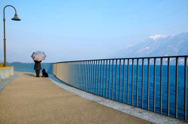海岸一个人带着伞和一条狗站在海边码头上的美丽景色风景船天空