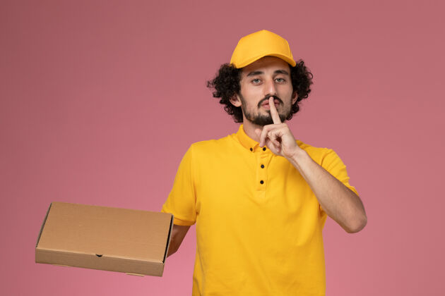 男性快递正面图：身穿黄色制服的男快递员拿着食品快递箱站在浅粉色的墙上快递专业送货