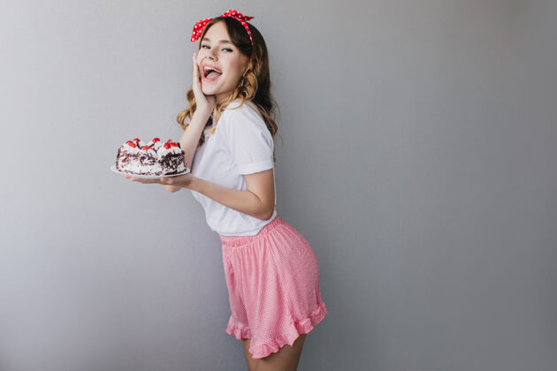 有趣穿粉红色裙子的年轻漂亮女人庆祝生日热情的黑发女孩拿着甜蛋糕跳舞可爱味道模特