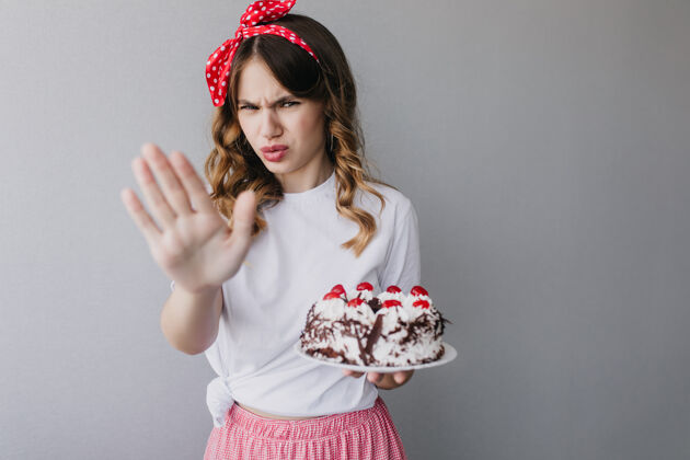 美式室内画像：不幸的女人戴着红丝带和蛋糕摆姿势生日女孩拿着馅饼甜点欧式蛋糕