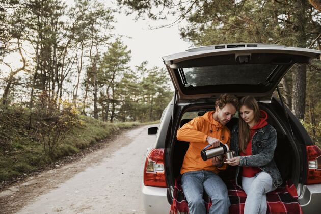 水平可爱的夫妇在汽车后备箱里享受热饮料饮料户外远足