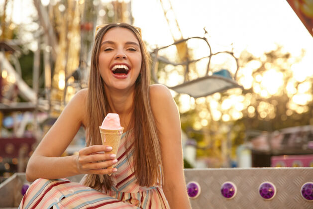 快乐快乐的年轻可爱的女人的肖像 戴着太阳镜在户外的景点公园里摆姿势 笑着张开大嘴 手里拿着冰淇淋筒美丽太阳镜心情