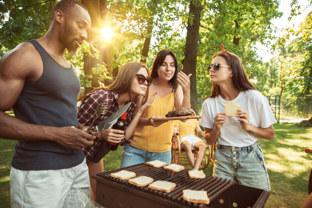 午餐一群快乐的朋友在阳光明媚的日子里举行啤酒和烧烤聚会野餐喝酒年轻