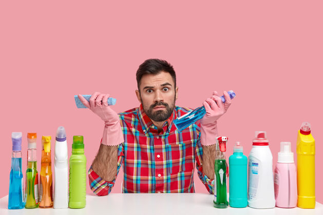 洗涤剂照片中的大胡子男人穿着格子衬衫 用不同的清洁材料 周围是塑料瓶 看起来令人惊讶整洁凝视瓶子