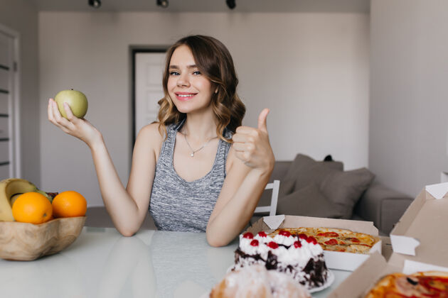 微笑美丽的白人女孩享受她的饮食与新鲜水果令人惊叹的女人在苹果和蛋糕之间选择室内肖像家美丽巧克力