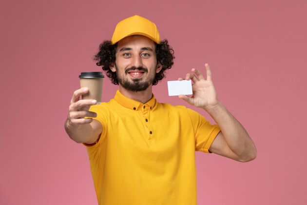 粉色正面图：身穿黄色制服 披风的男性快递员手持咖啡杯和粉色墙上的卡片咖啡名片工作
