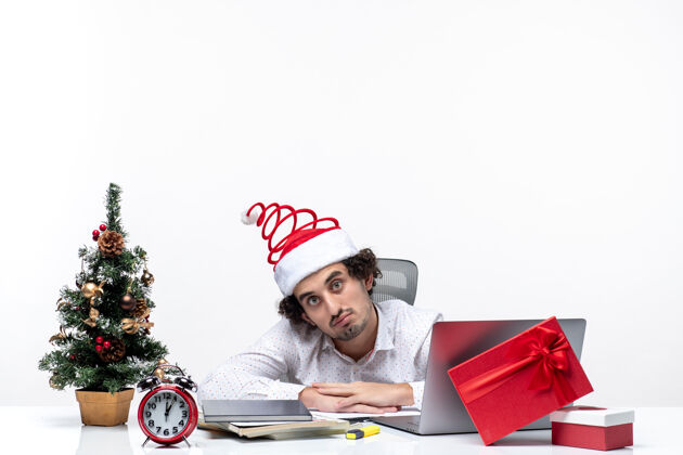 帽子新年心情与困惑的年轻商人与有趣的圣诞老人帽子感到惊讶 在白色背景的办公室人惊讶成年人
