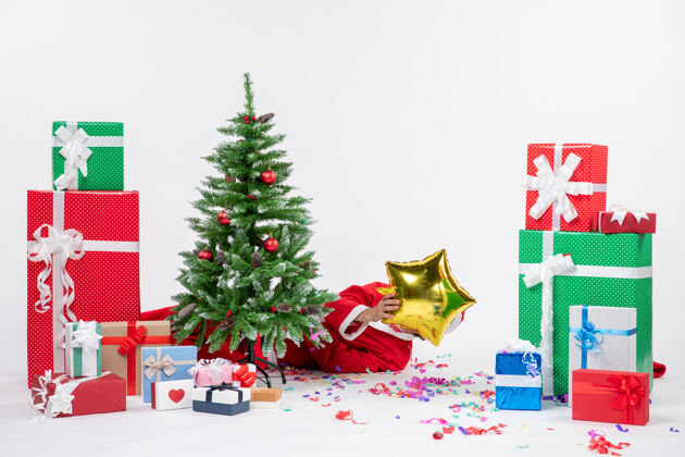 谎言圣诞老人躺在圣诞树后 在白色背景上不同颜色的礼物旁边合上了脸 这是节日的气氛礼物圣诞树不同